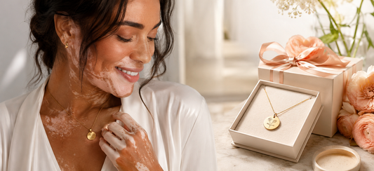 Femme avec vitiligo portant un bijou personnalisé doré dans une ambiance lumineuse et élégante, avec un coffret cadeau raffiné en arrière-plan.